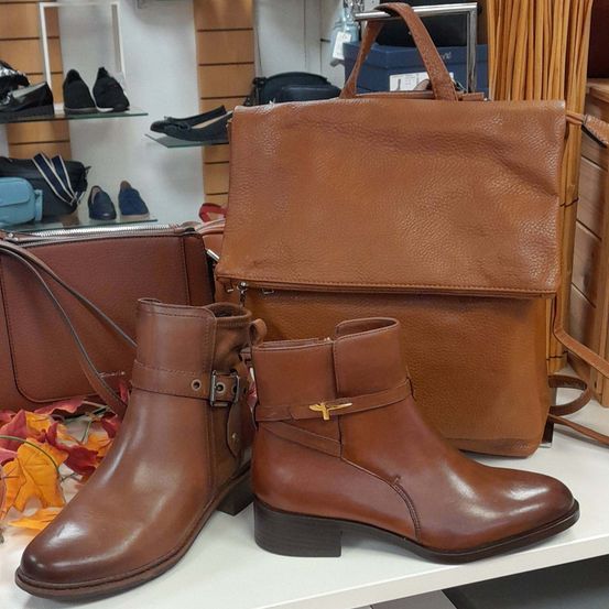 Ein Paar braune Lederstiefel mit Schnallen und eine braune Lederhandtasche sind auf einem weißen Tisch ausgestellt.