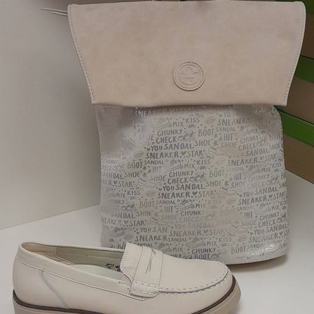 Ein Paar weiße Leder-Loafer und eine cremefarbene Lederhandtasche mit verschiedenen schuhbezogenen Wörtern bedruckt. Die Handtasche hat ein Logo auf der Vorderseite und steht auf einer weißen Oberfläche.