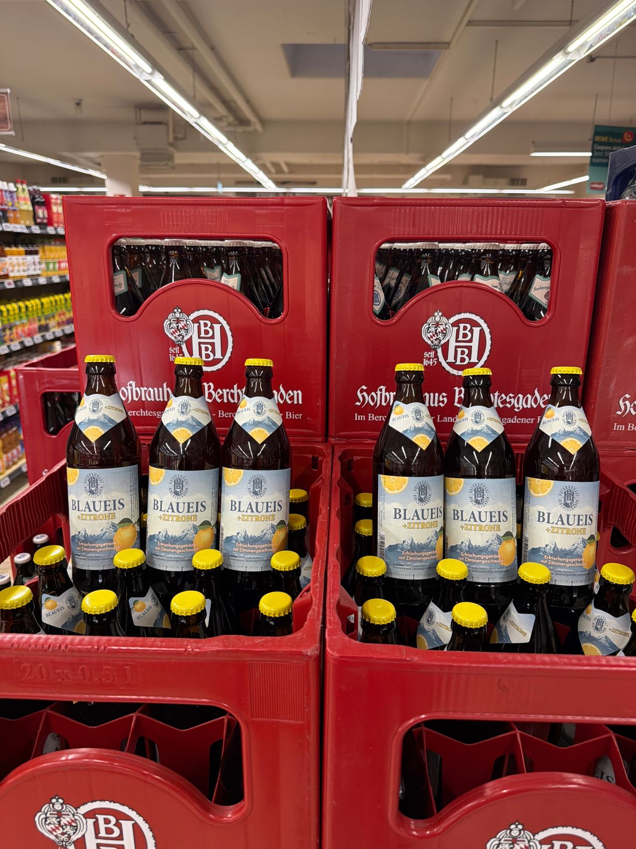 Reihen von Flaschen des Blaueis+Zitrone Bieres in roten Kisten in einem Supermarkt, mit gelben Kappen und blauen Etiketten.