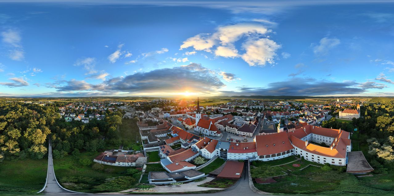 Luftaufnahme einer Stadt mit Gebäuden mit roten Dächern, vor dem Hintergrund eines Sonnenuntergangs mit blauem Himmel und Wolken.