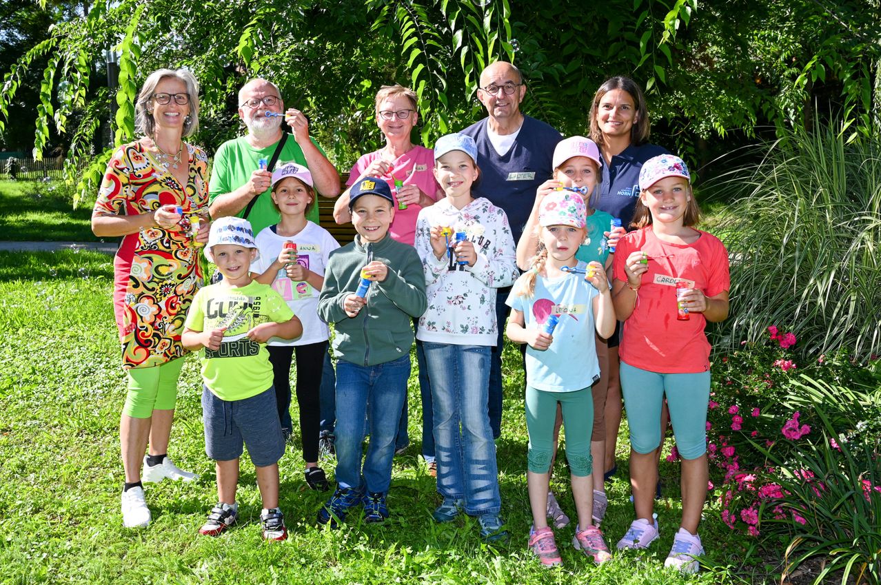 Eine Gruppe von Erwachsenen und Kindern posiert für ein Foto im Garten. Sie alle halten Seifenblasenmacher in den Händen, lächeln und schauen zur Kamera.