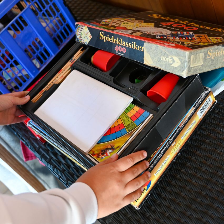 Eine Hand öffnet eine Schachtel eines Brettspiels mit Würfeln und Karten auf einem schwarzen Tisch.