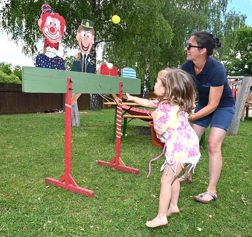 Eine Frau hilft einem kleinen Mädchen, auf ein Clown-Ziel in einer Hinterhof-Spieleinrichtung zu zielen.