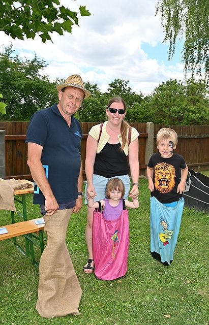 Eine vierköpfige Familie steht auf einem Rasen. Ein Mann und eine Frau halten Händchen mit zwei Kindern. Sie alle lächeln.