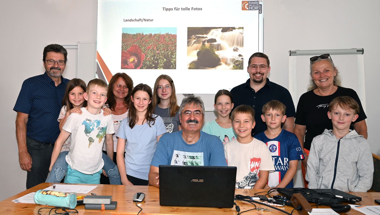 Gruppenfoto mit einem Mann und mehreren Kindern und Frauen in einem Klassenzimmer vor einem Bildschirm mit Fototipps.