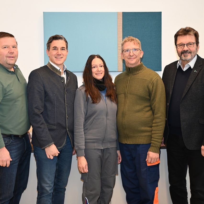 Fünf Personen, darunter eine Frau, stehen gemeinsam vor einer weißen Wand. Sie scheinen für ein Foto zu posieren.