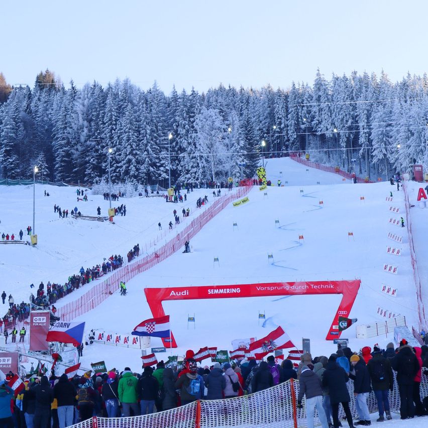 Eine Skipiste mit Zuschauern, die einen Wettkampf verfolgen, gesponsert von Audi, mit Flaggen verschiedener Länder.
