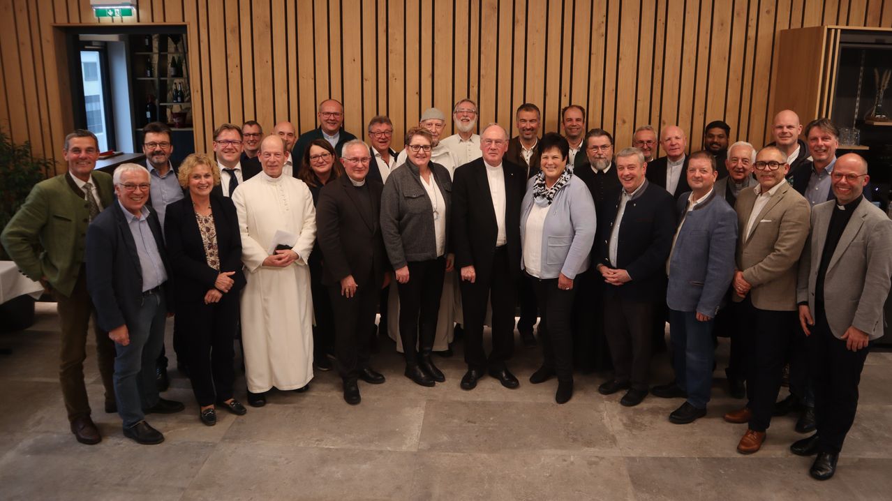 Eine Gruppe von Menschen, darunter Geistliche und Laien, posiert für ein Foto vor einer Holzwand.