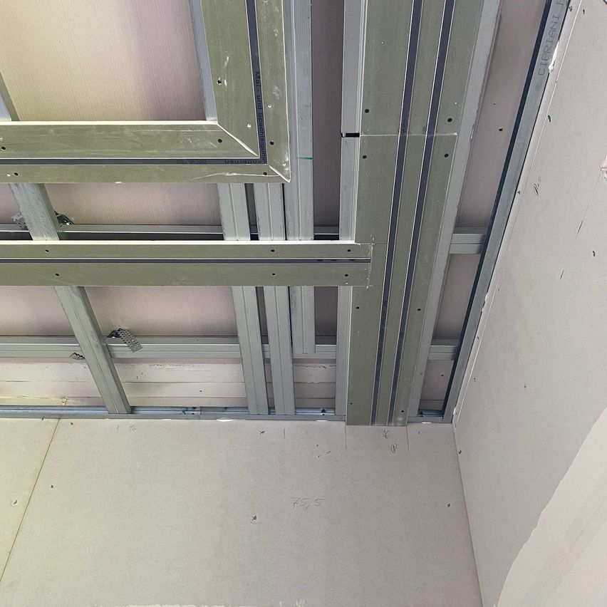 Close-up of a room's interior with exposed metal ceiling beams and unfinished walls.