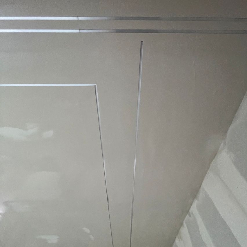 A white ceiling with three silver stripes, one vertical and two horizontal. A light source reflects off the ceiling.