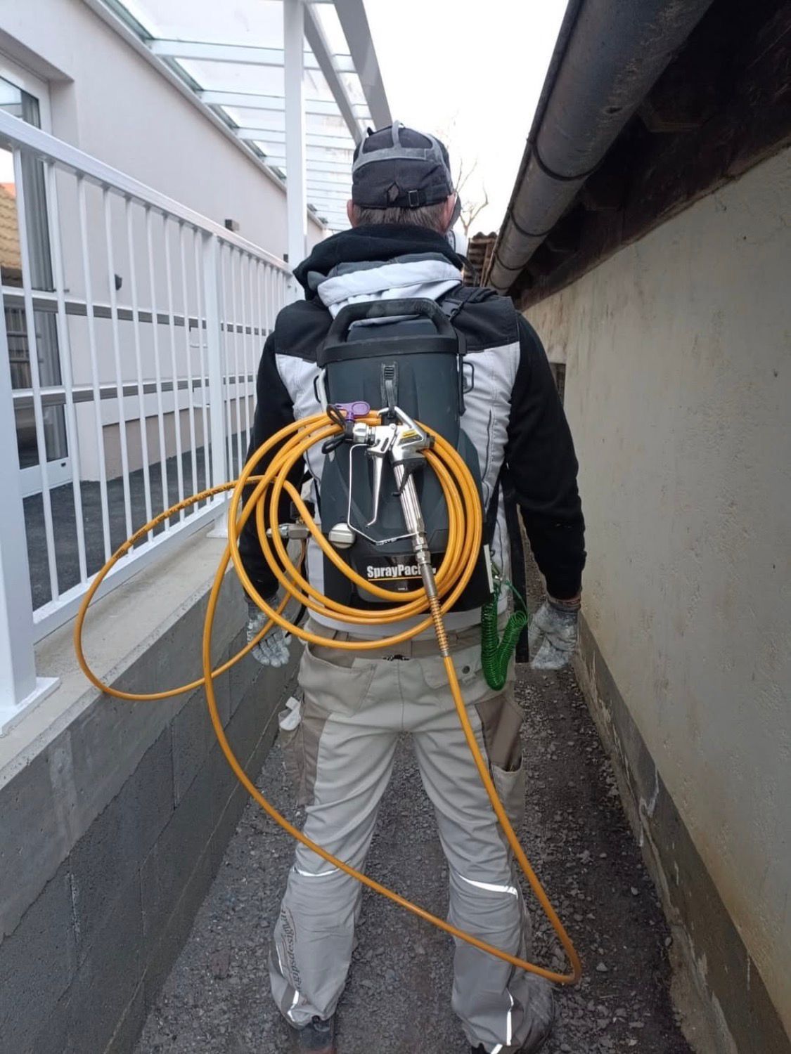 Ein Mann geht einen Pfad hinunter und trägt einen Rucksack mit einem daran befestigten gelben Schlauch. Der Schlauch ist mit einem Sprühgerät verbunden.