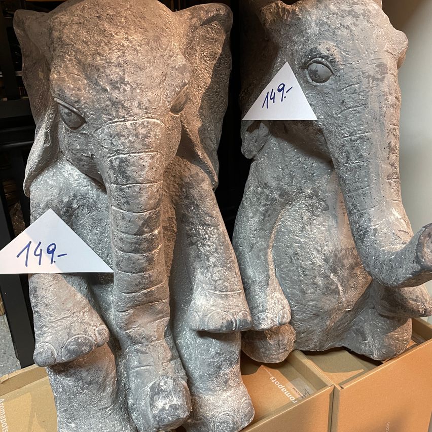 Zwei graue Elefantenstatuen aus Stein sind auf Kisten gestapelt. Beide haben Preisschilder: 149- auf der linken und 149 auf der rechten.