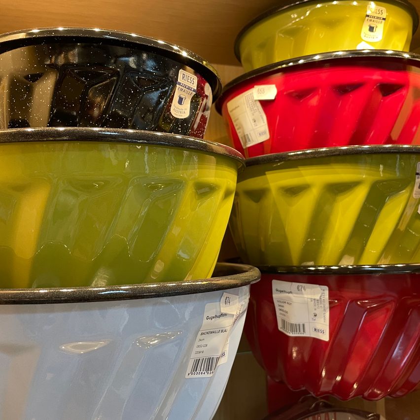 A stack of colorful enamel bowls with labels and barcodes, including green, red, and yellow, displayed on a wooden surface.