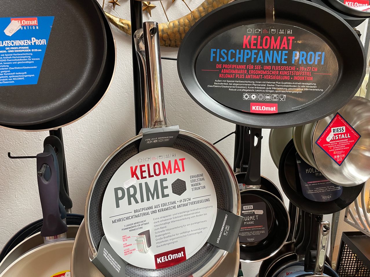 A stainless steel cooking pan labeled 'Keelomat Prime' is displayed with other cookware. The pan is made of stainless steel and has a non-stick coating. It is part of a larger set of kitchen utensils.