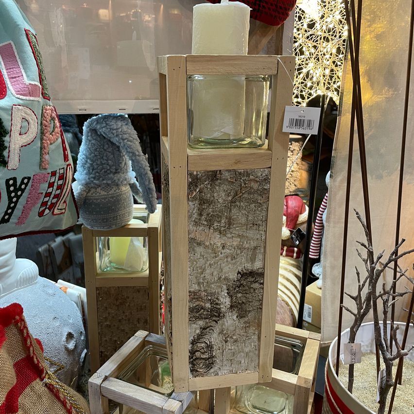 A wooden candle holder with a birch bark design and a white candle inside stands in a store, surrounded by other decorative items.