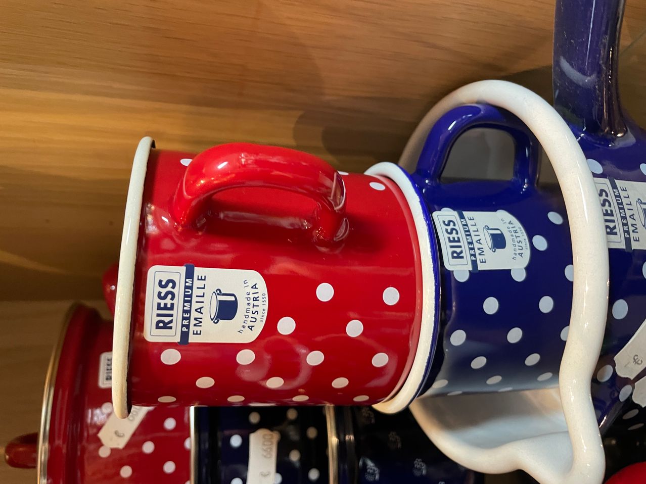Zwei Emaille-Becher mit Punkten. Der obere Becher ist rot und der untere blau. Beide haben Henkel und stehen auf einer Holzoberfläche.