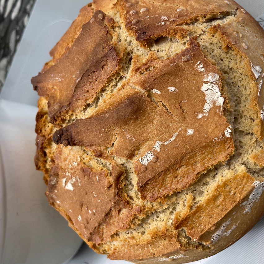 Ein Laib Artisan-Brot mit knuspriger Kruste, braun und goldbraun in der Farbe, auf einer weißen Oberfläche platziert. Das Brot hat einige Risse und einen leicht verbrannten Fleck.