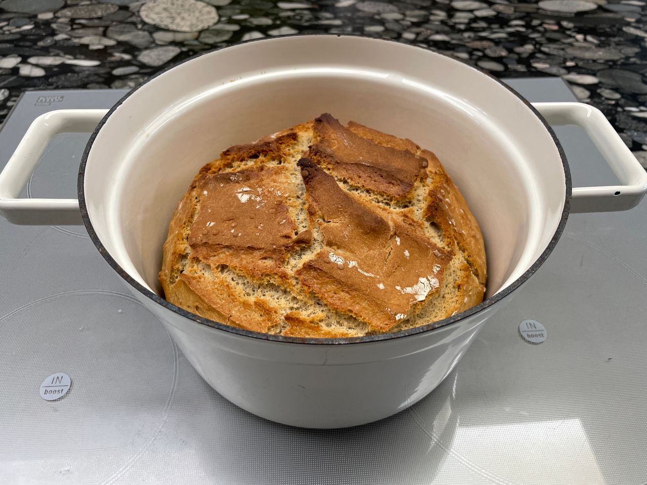 Ein Laib Brot in einem weißen Topf, wahrscheinlich zum Backen bereit, steht auf einem Herd.