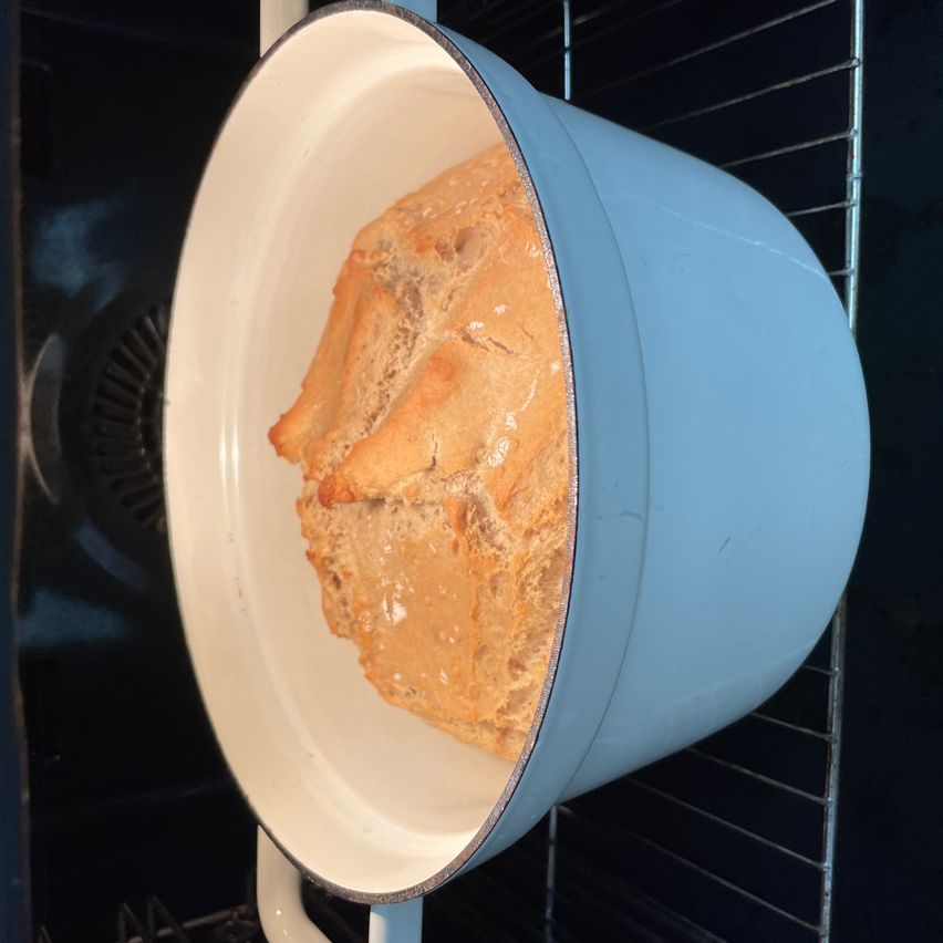 Eine Nahaufnahme eines blauen Topfes mit einem goldbraunen Brot darin, im Ofen stehend.