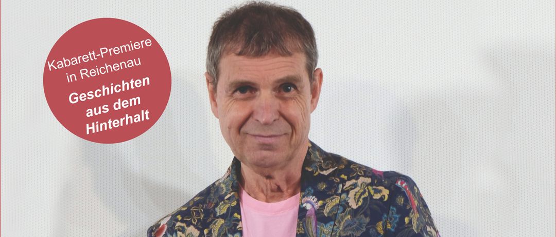 Ein Mann in einem farbenfrohen Jackett mit einem rosa T-Shirt darunter steht lächelnd für ein Foto. Der Hintergrund ist weiß mit einem roten Kreis mit dem Text 'Kabaret-Premiere in Reichenau Geschichten aus dem Hinterhalt'. Das Datum '09.11.2025' und die Zeit '18 Uhr' sind ebenfalls erwähnt.