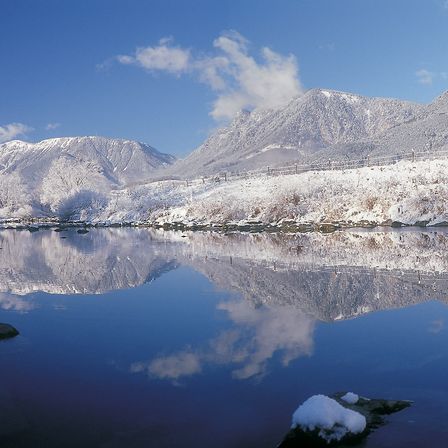 Eine friedliche Winterlandschaft mit schneebedeckten Bergen, die sich in einem ruhigen See spiegeln, unter einem klaren blauen Himmel.