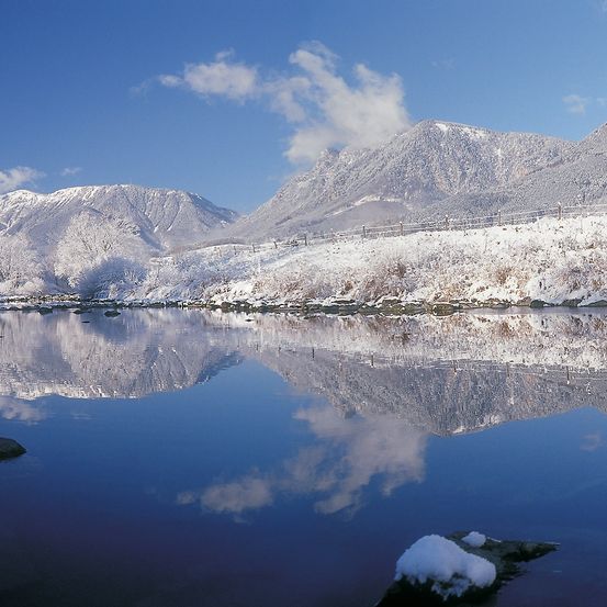 Eine friedliche Winterlandschaft mit schneebedeckten Bergen, die sich in einem ruhigen See spiegeln, unter einem klaren blauen Himmel.