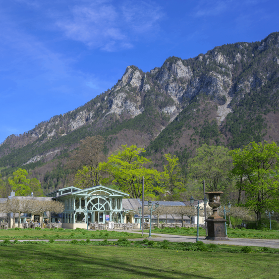 Ein malerisches Café liegt am Fuße eines Berges mit üppigem Grün. Bäume und Berge sind im Hintergrund zu sehen.