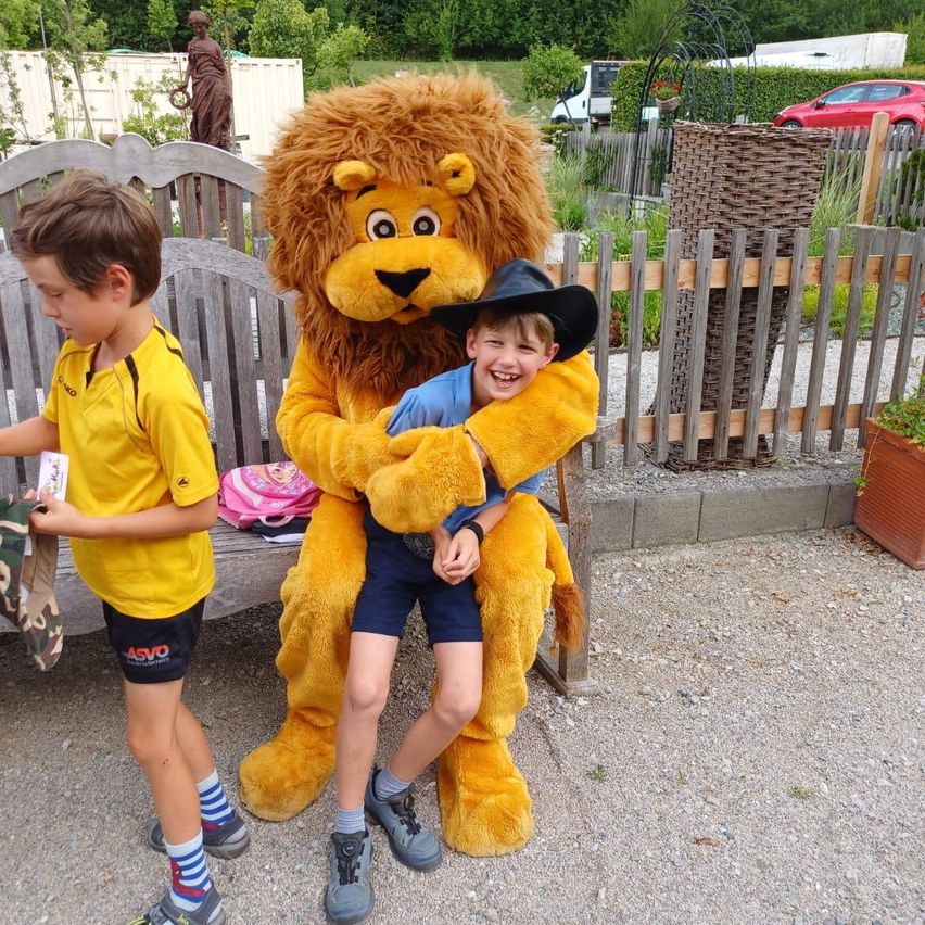 Zwei Jungen stehen neben einer Holzbank; ein Junge in einem Löwenkostüm umarmt einen Jungen mit einem Cowboyhut.