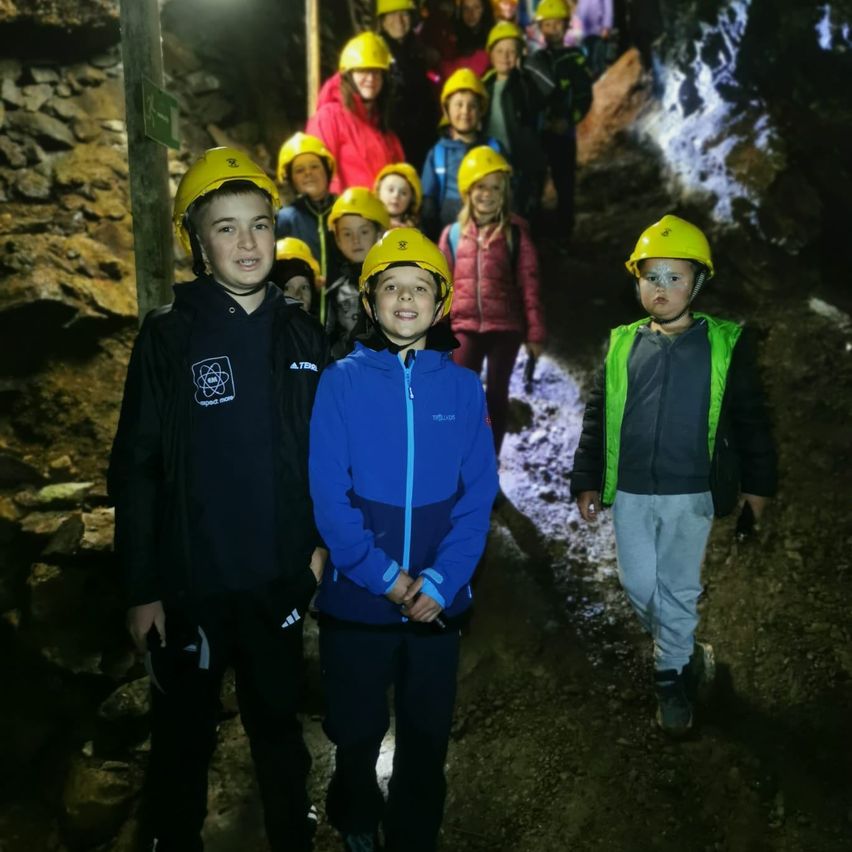 Eine Gruppe von Kindern mit Helmen erkundet eine Höhle, einige stehen, andere gehen auf einem felsigen Pfad.
