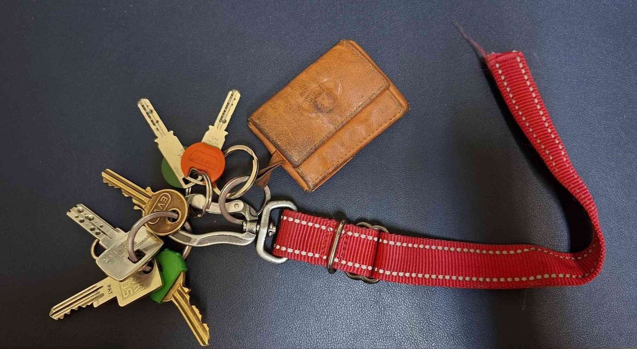 A brown leather wallet with multiple keys attached to a red lanyard on a blue surface.