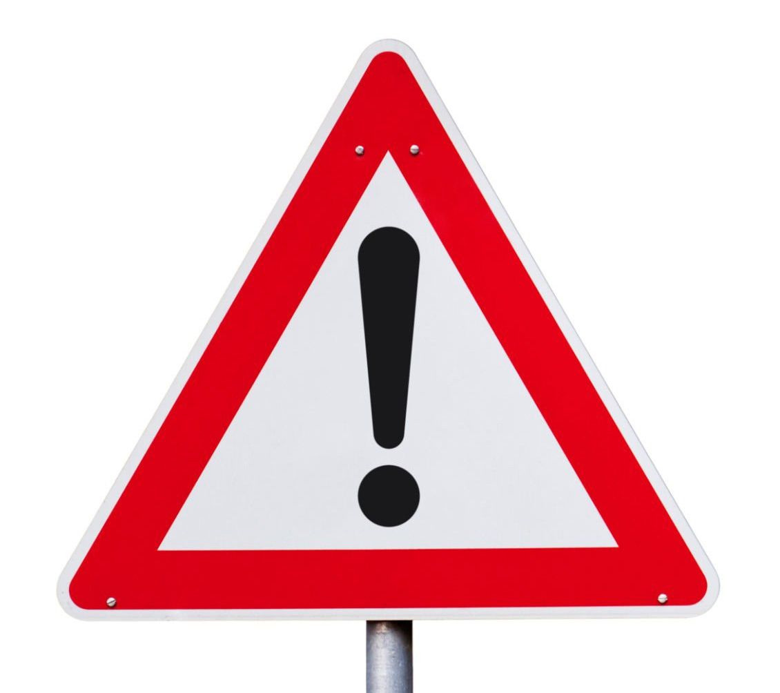 A red and white triangular sign with a black exclamation mark in the center. It stands on a pole against a white background.