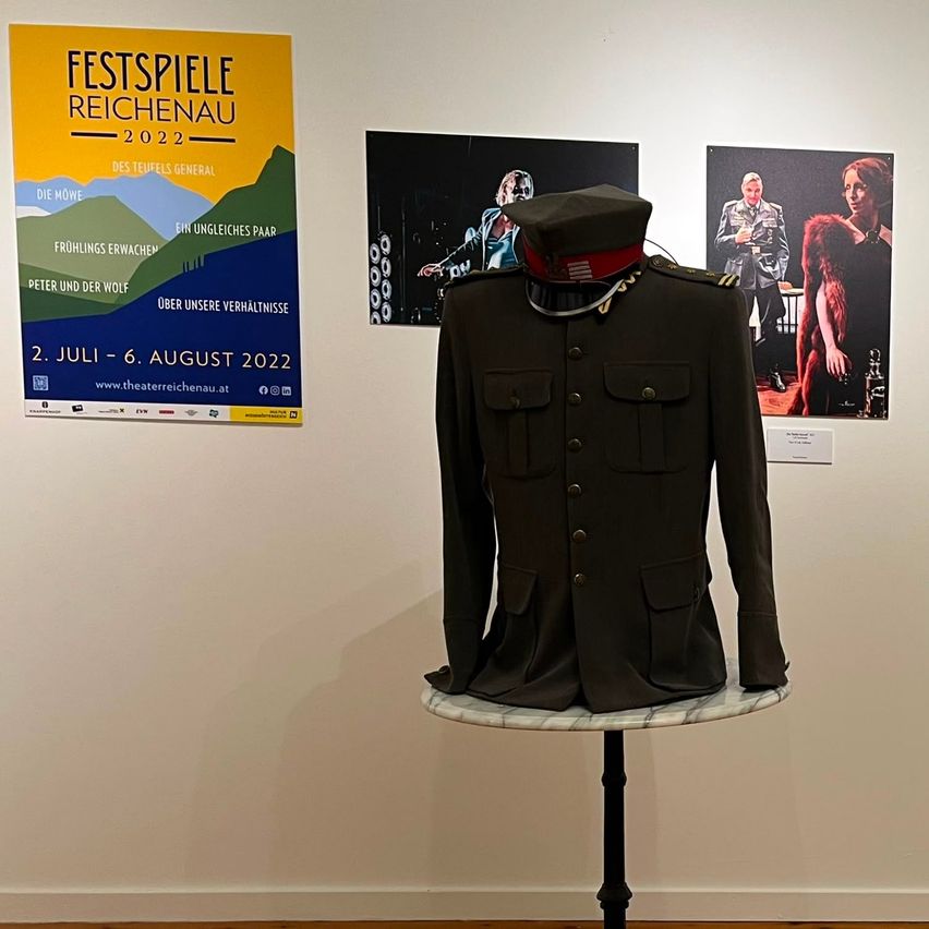 A military uniform is displayed on a pedestal in front of a wall with posters for the Reichenau Festival 2022.