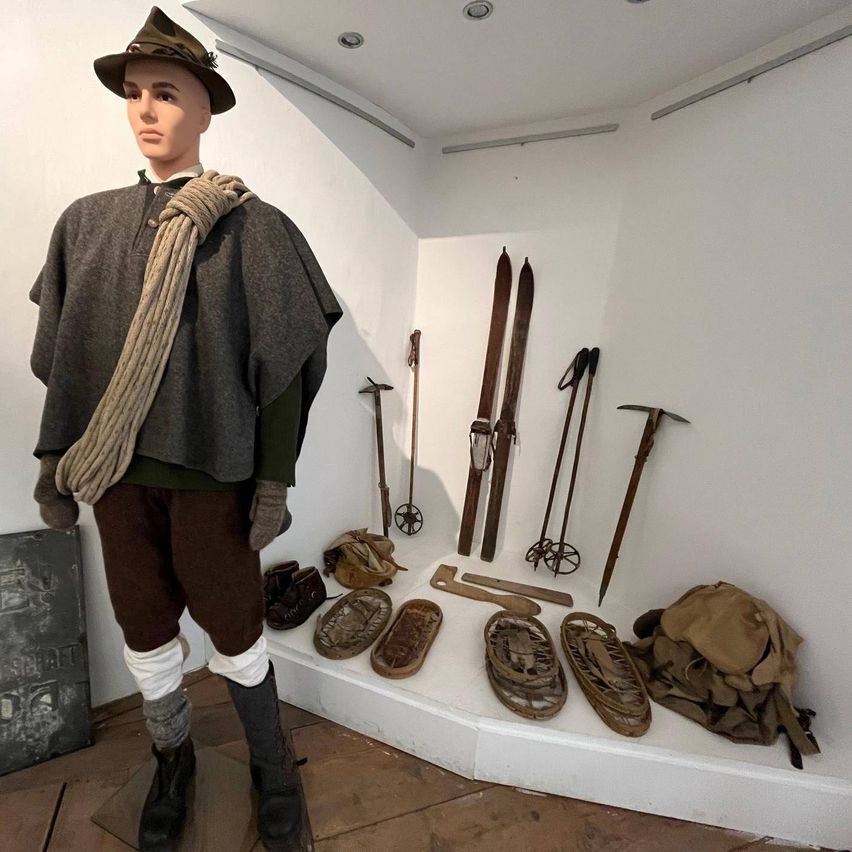 A mannequin dressed in historical mountaineering gear stands in a room with white walls, displaying various mountaineering tools.