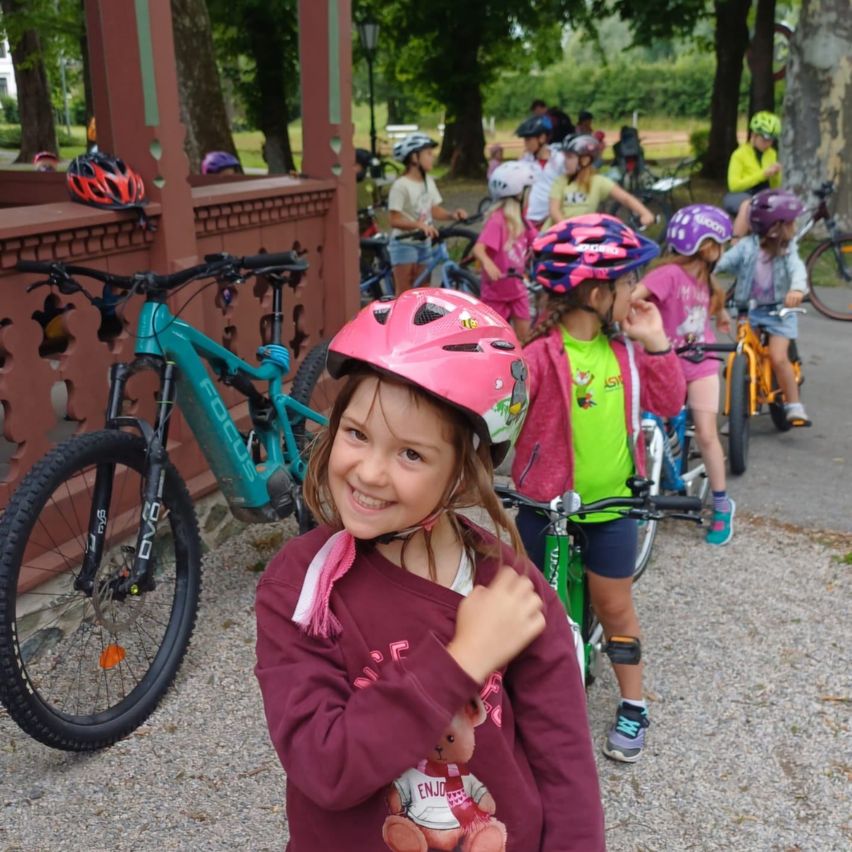 Eine Gruppe von Kindern in Helmen und Fahrradausrüstung steht draußen mit ihren Fahrrädern, lächelt und posiert für ein Foto.