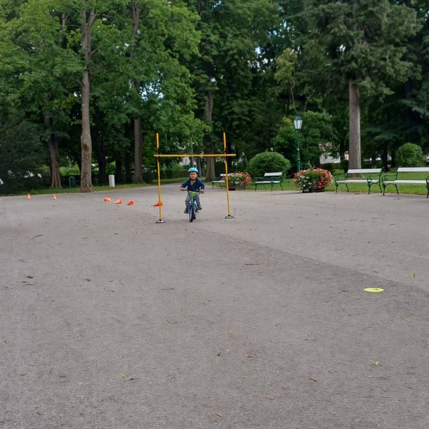 Ein junger Junge fährt mit seinem Fahrrad durch einen Park und navigiert um orangefarbene Kegel und einen gelben Hindernisparcours herum.