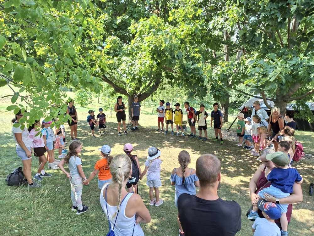 Kindergruppe mit Betreuern steht im Kreis unter Bäumen auf einer Wiese in Niederösterreich