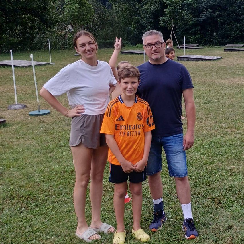 Familie steht im Freien auf einer Wiese, Mann mit Brille, Frau mit erhobener Hand, Junge im Fußballtrikot