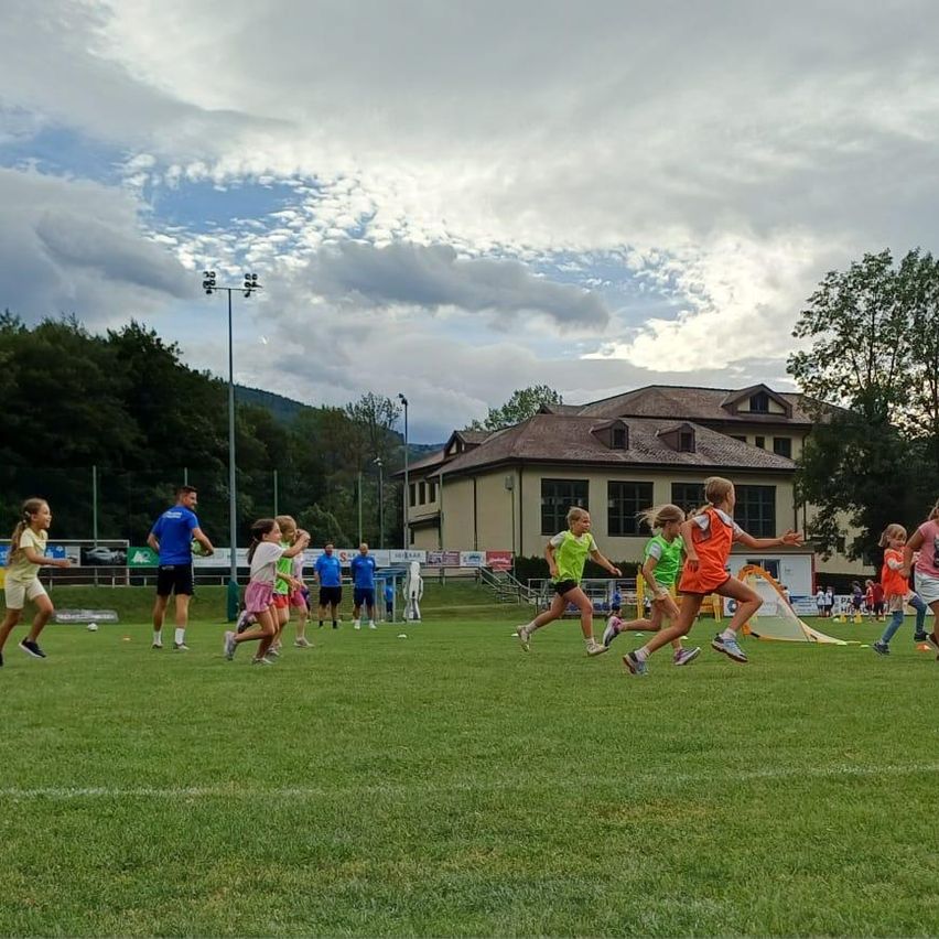 Kinder rennen auf einem Sportplatz in Österreich, Mädchen in bunten Trikots, Trainer im Hintergrund