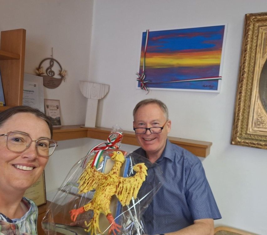 Mann mit Brille und Frau lächeln mit gelbem Vogelgeschenk in einem Raum mit Bildern.