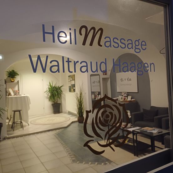 Ein Massagestudio namens 'Heilmassage Waltraud Haagen'. Das Innere besteht aus einem Tisch, einem Hocker, Topfpflanzen, einer Couch und einem Kaffeetisch mit Büchern.