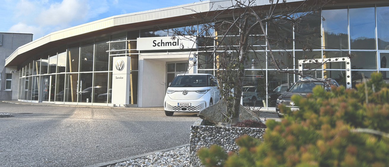 Ein weißer Volkswagen ID.3 ist vor einem Gebäude namens Schmal geparkt. Das Gebäude hat Glaswände und Türen und ein Schild mit dem Volkswagen-Logo.
