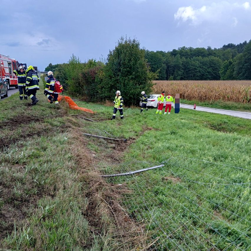 Rettungskräfte in gelben und roten Uniformen kümmern sich um einen Vorfall am Straßenrand, ein Auto in der Nähe und ein Feuerwehrwagen geparkt am Straßenrand.