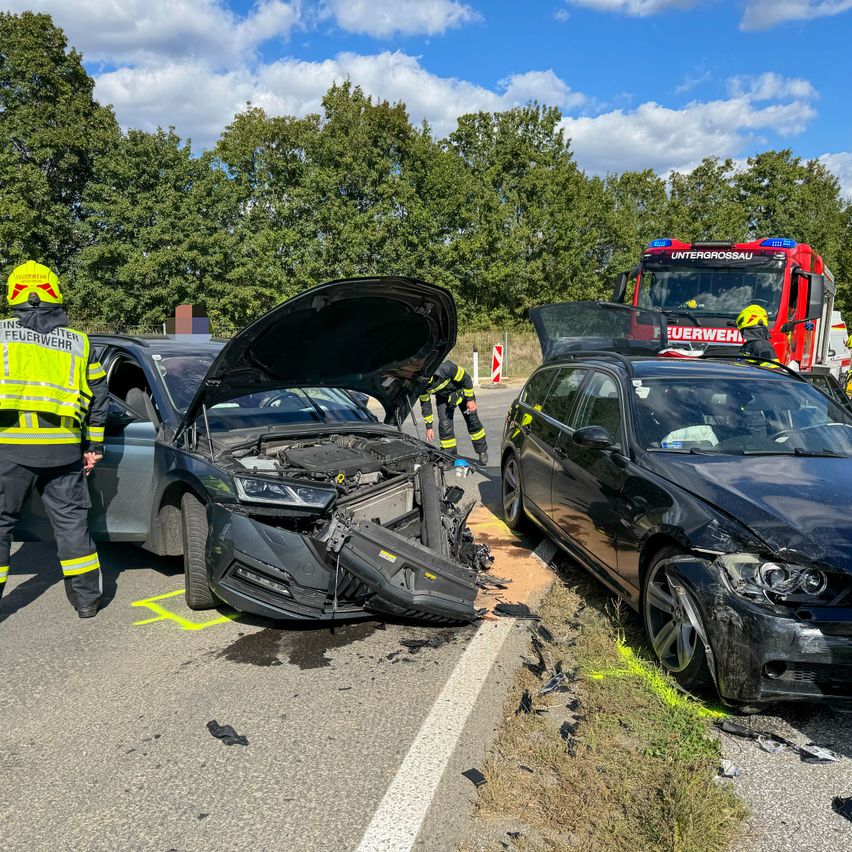Rettungskräfte inspizieren ein beschädigtes Auto am Straßenrand, mit einem weiteren Auto in der Nähe und einem Feuerwehrfahrzeug im Hintergrund.