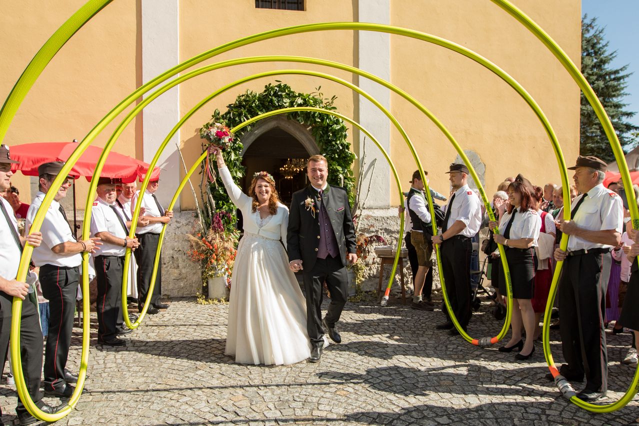 Ein Brautpaar geht durch einen gelben Bogen auf ihrer Hochzeit, umgeben von Gästen.