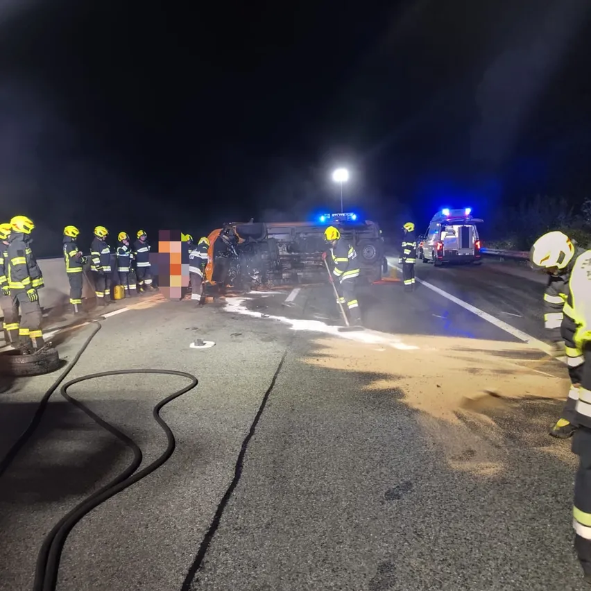 Eine Gruppe von Feuerwehrleuten steht nachts auf einer Autobahn und kümmert sich um ein demoliertes Fahrzeug.