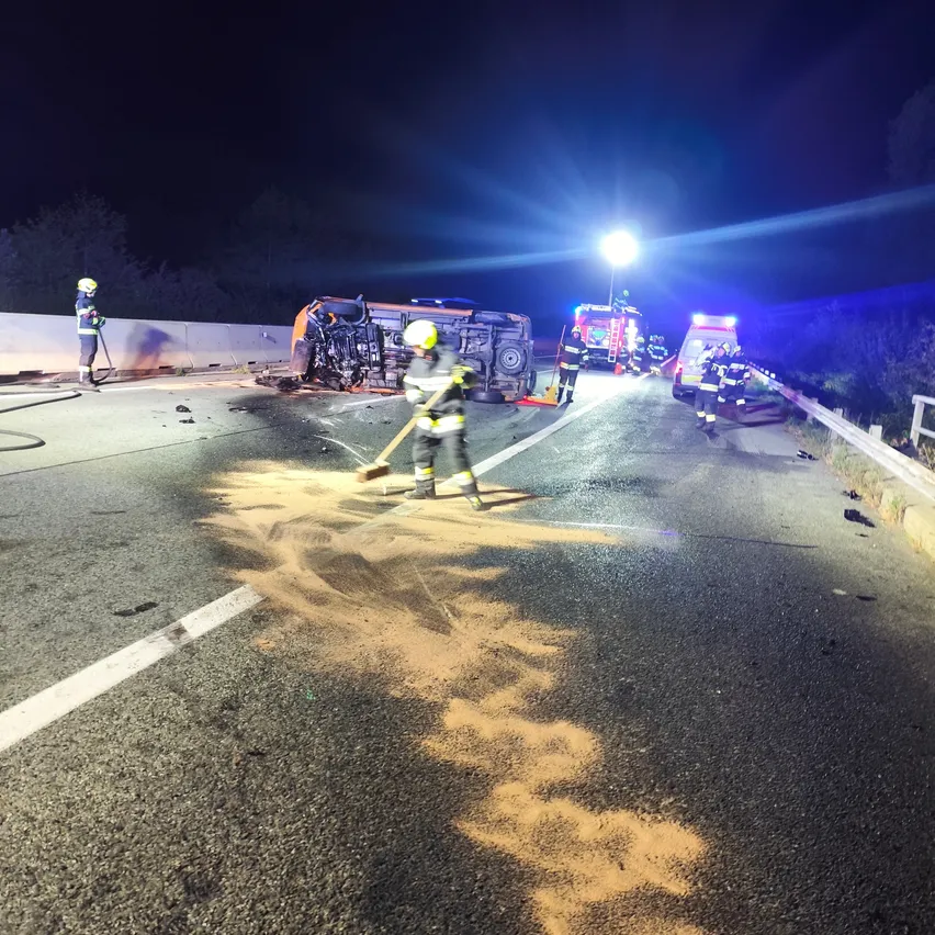 In der Nacht, eine Unfallstelle mit einem umgekippten Fahrzeug und Rettungsdiensten auf der Straße.