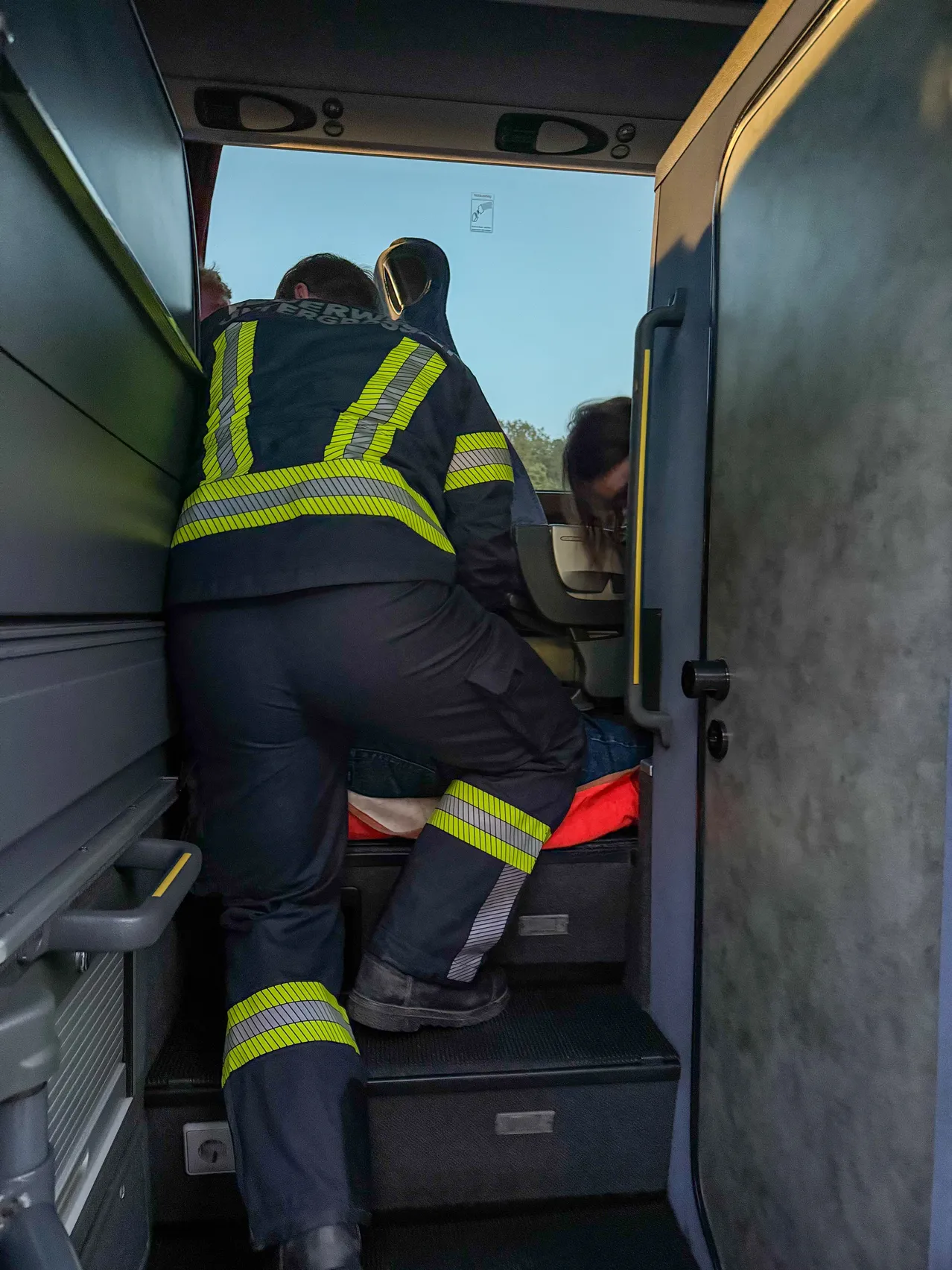 Ein Feuerwehrmann in einem gelben und schwarzen Uniform klettert die Stufen eines Fahrzeugs hinauf.