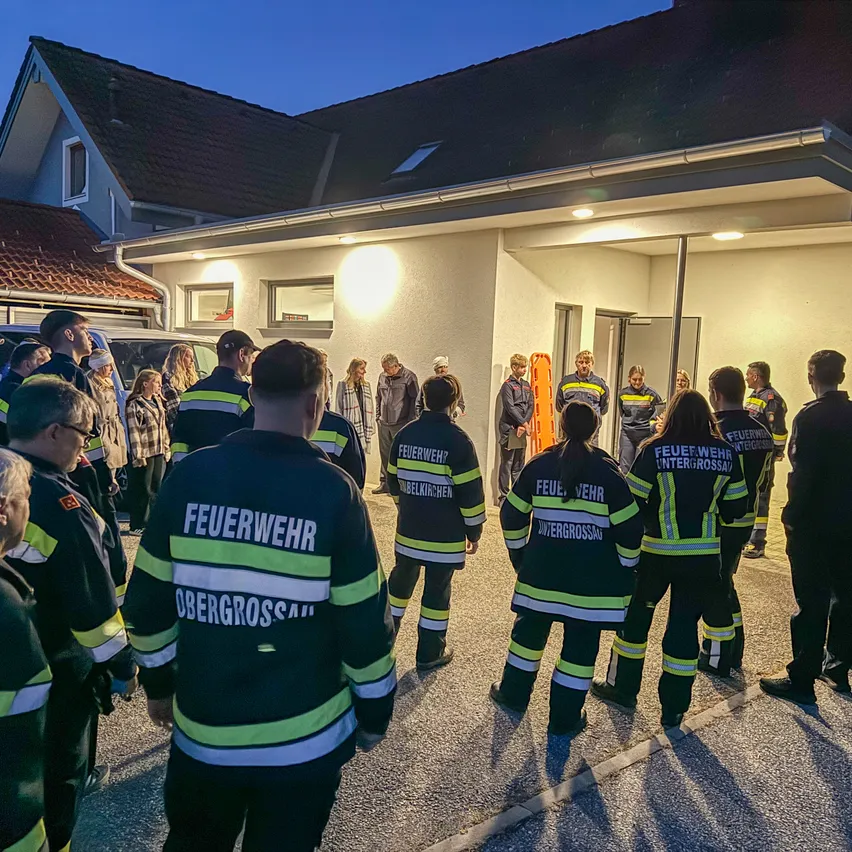 Eine Gruppe von Feuerwehrleuten steht nachts vor einem Haus.