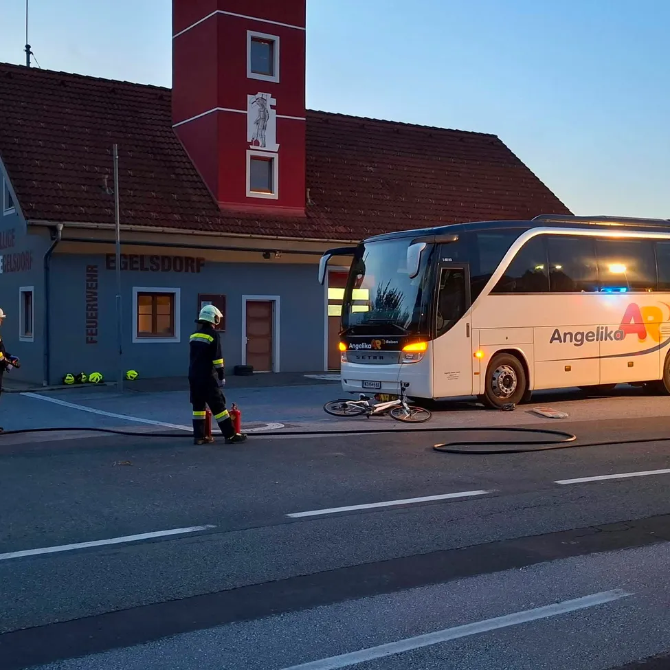 Ein Bus ist vor einem Gebäude mit einem Turm geparkt. Zwei Personen in Uniformen stehen neben dem Bus.
