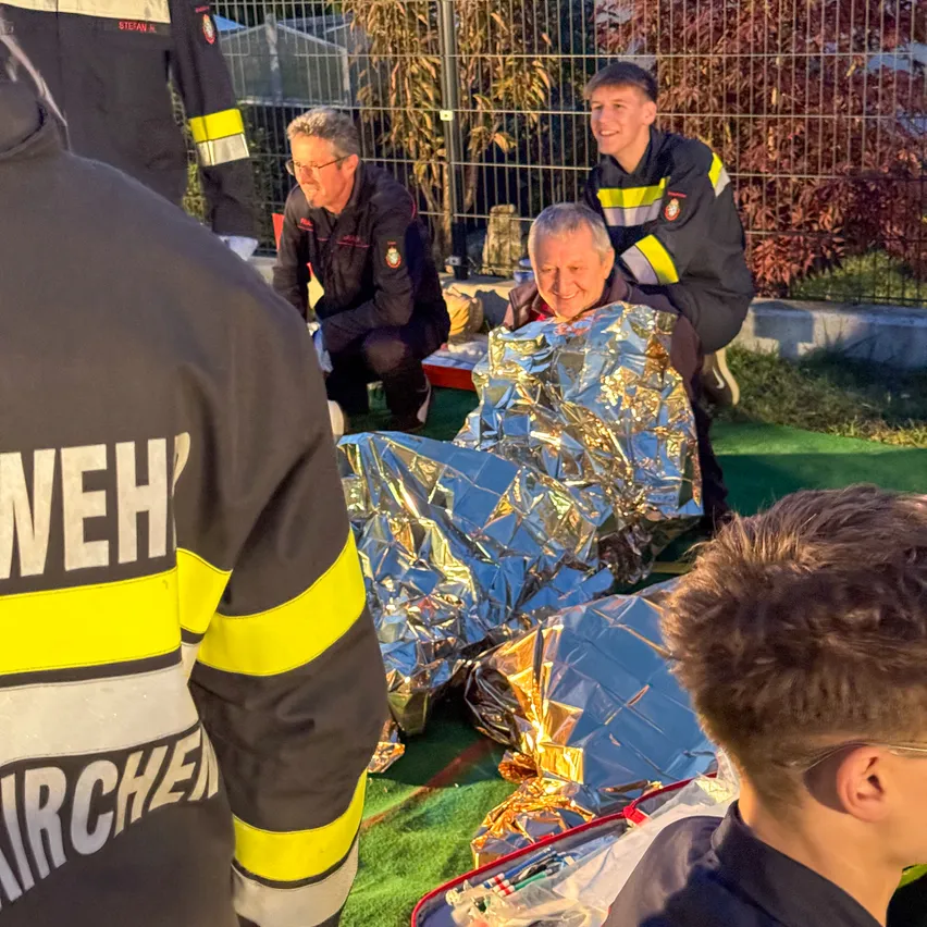 Eine Gruppe von Feuerwehrleuten versammelt sich um einen Mann, der in eine silberne Decke gewickelt ist.